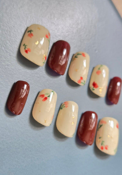 Ruby Meadow hand-painted red floral press-on nails on a cream base with gold foil accents